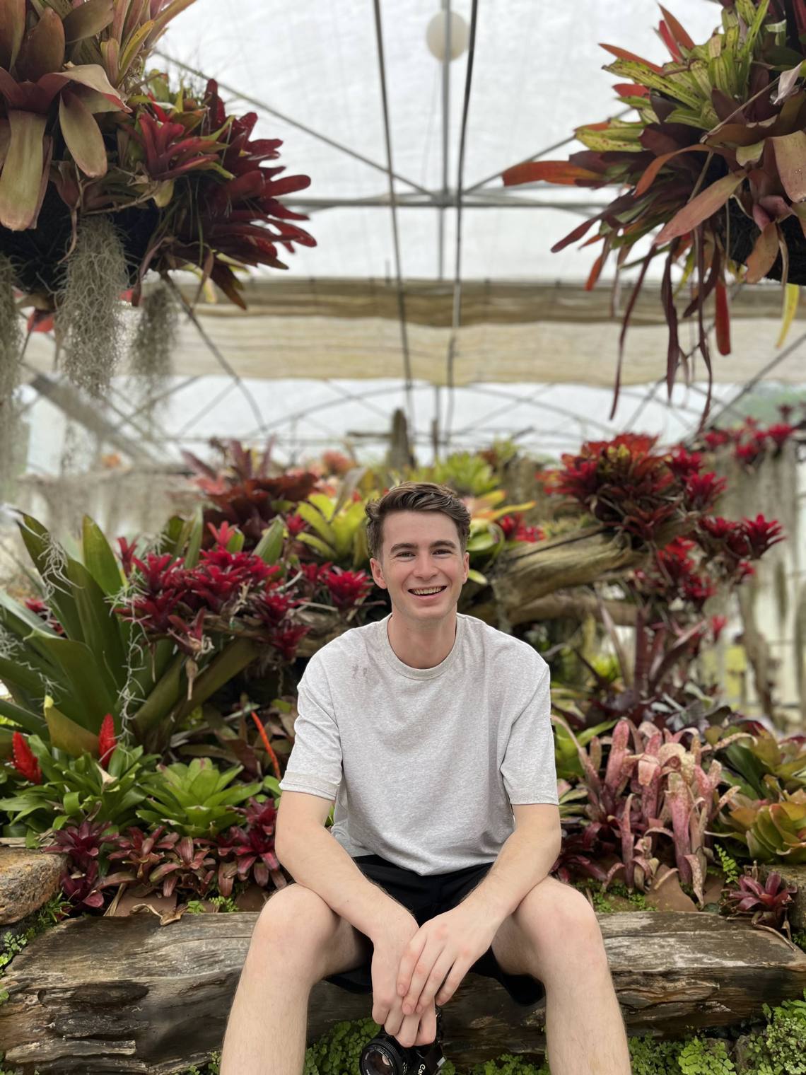 Stuart seated with a film camera in a Chiang Mai bromeliad greenhouse